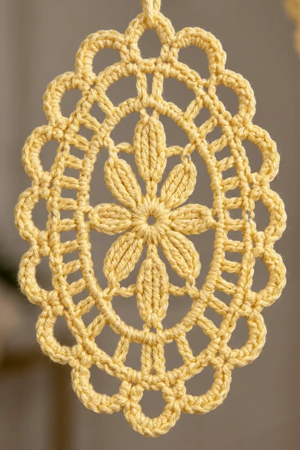 A delicate yellow crochet ornament featuring a flower center and intricate lace pattern hanging against a soft blurred background.