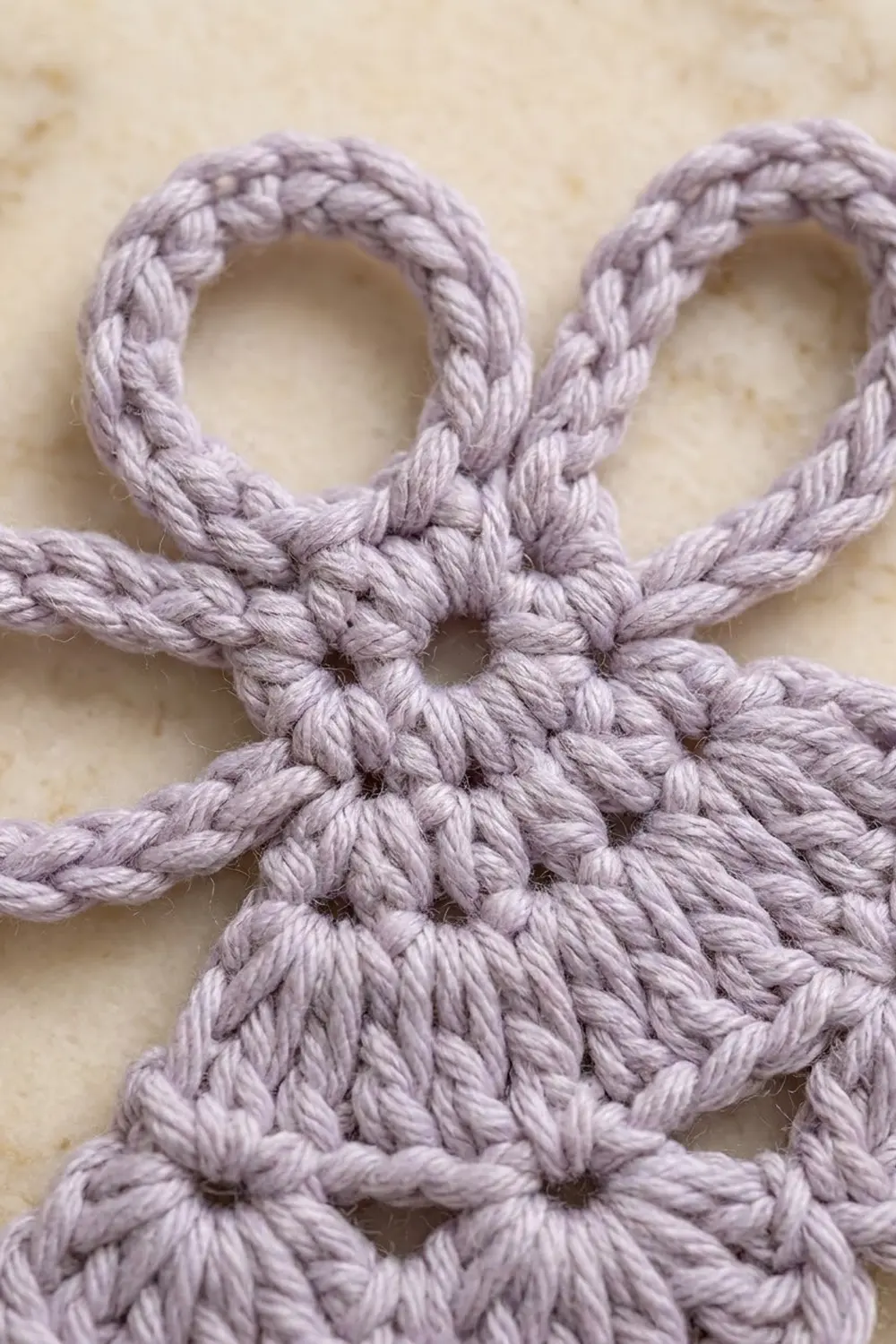 Close-up of a lavender macramé knot detail with twisted rope loops against a neutral beige background.