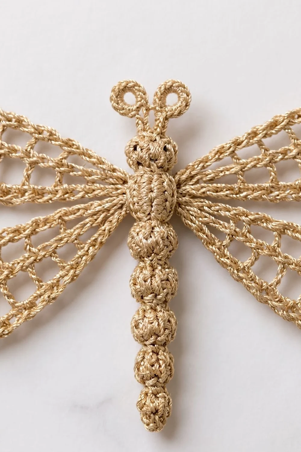 Crocheted dragonfly ornament made of golden twine with textured body and delicate openwork wings against white background.
