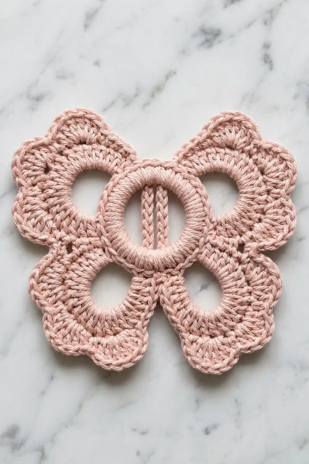 A delicate pink crocheted flower appliqué with six petals displayed on a white marble surface.