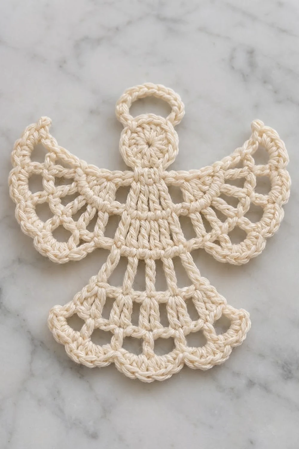 A cream-colored crocheted angel ornament with delicate lace wings and a loop for hanging on marble.