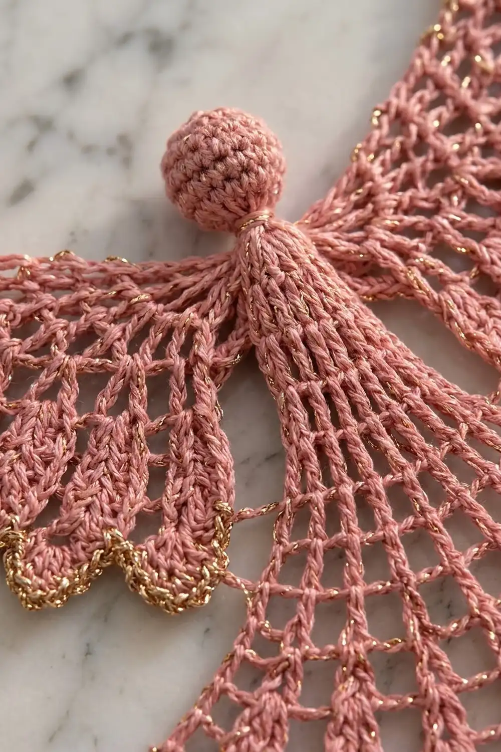 Crocheted pink angel ornament with gold accents displayed on a marble surface.