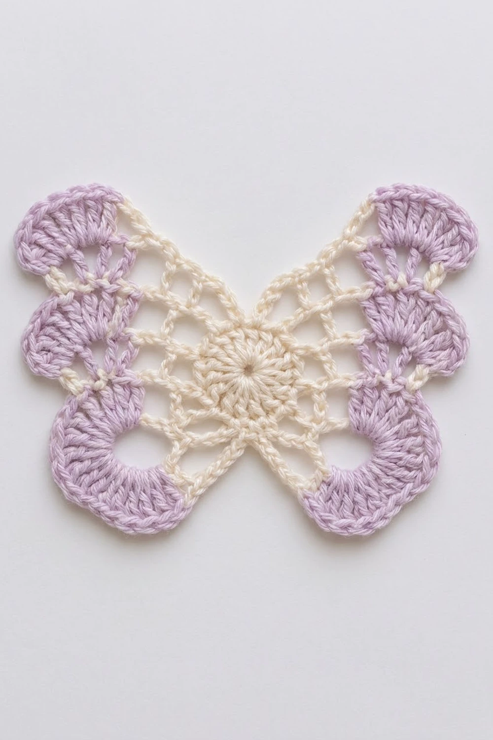 A crocheted butterfly appliqué in lavender and cream yarn displayed flat on a white background.