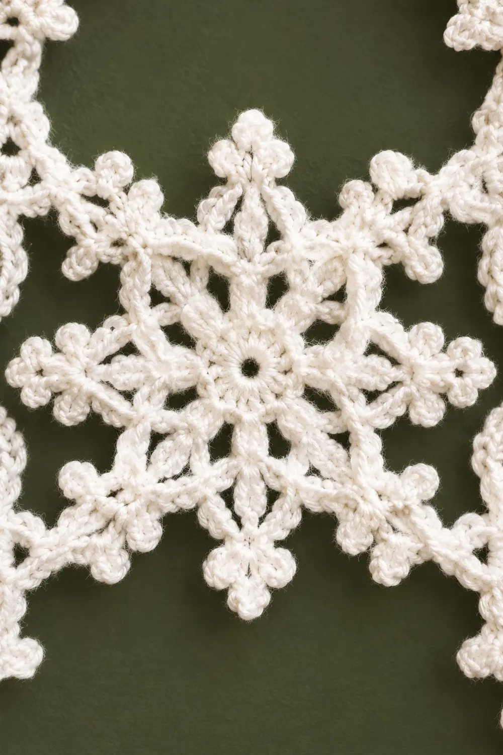 Delicate white crocheted snowflake ornament with intricate looped patterns displayed against a soft green background.
