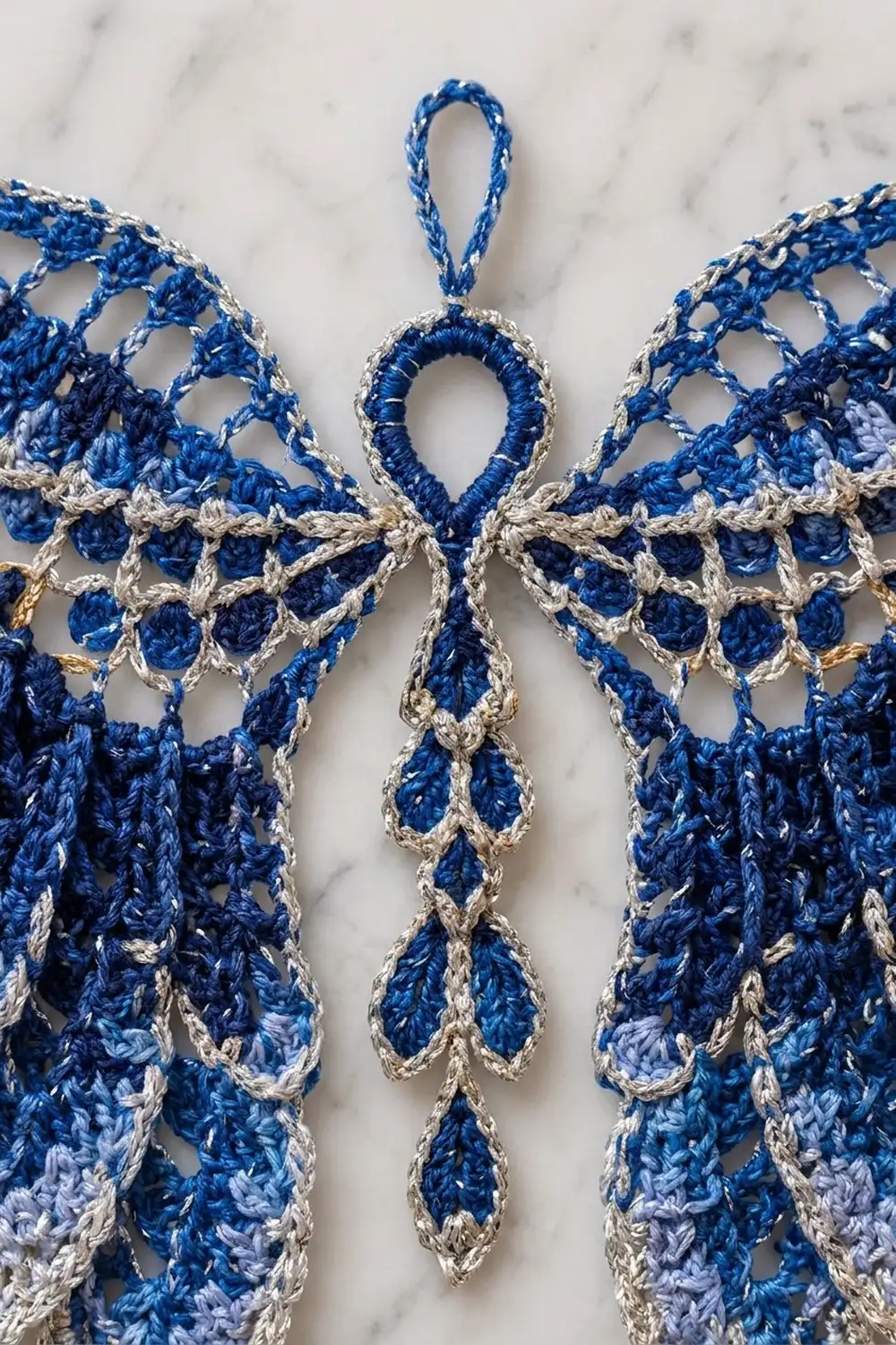 Crocheted angel ornament in blue and cream yarn displayed on white marble surface.