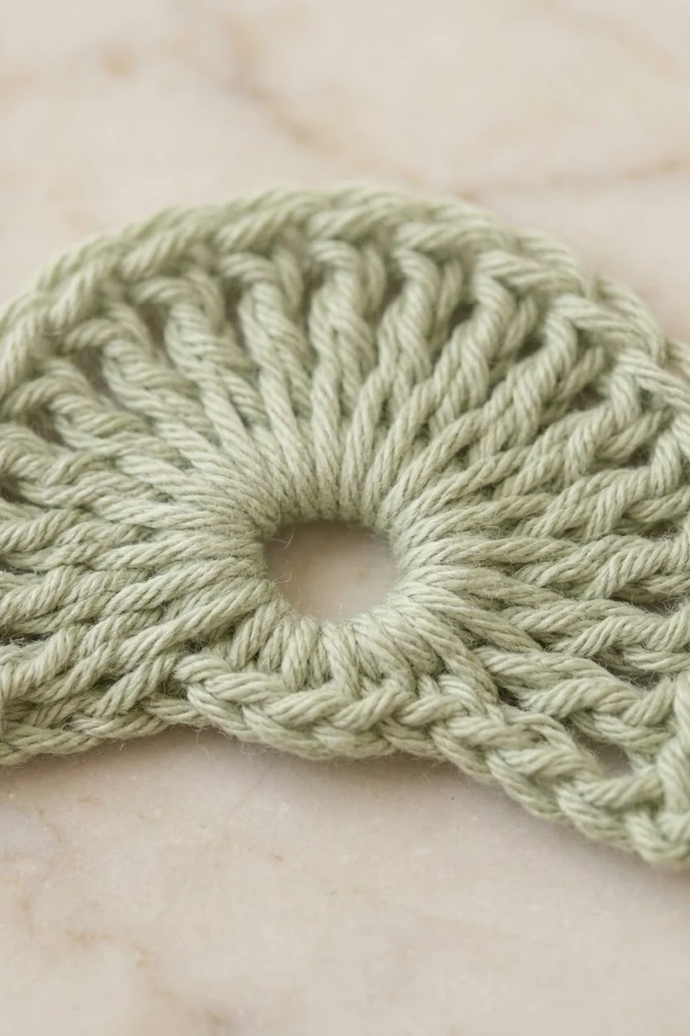 Coiled pale green twisted rope arranged in a circular loop on a light beige surface.