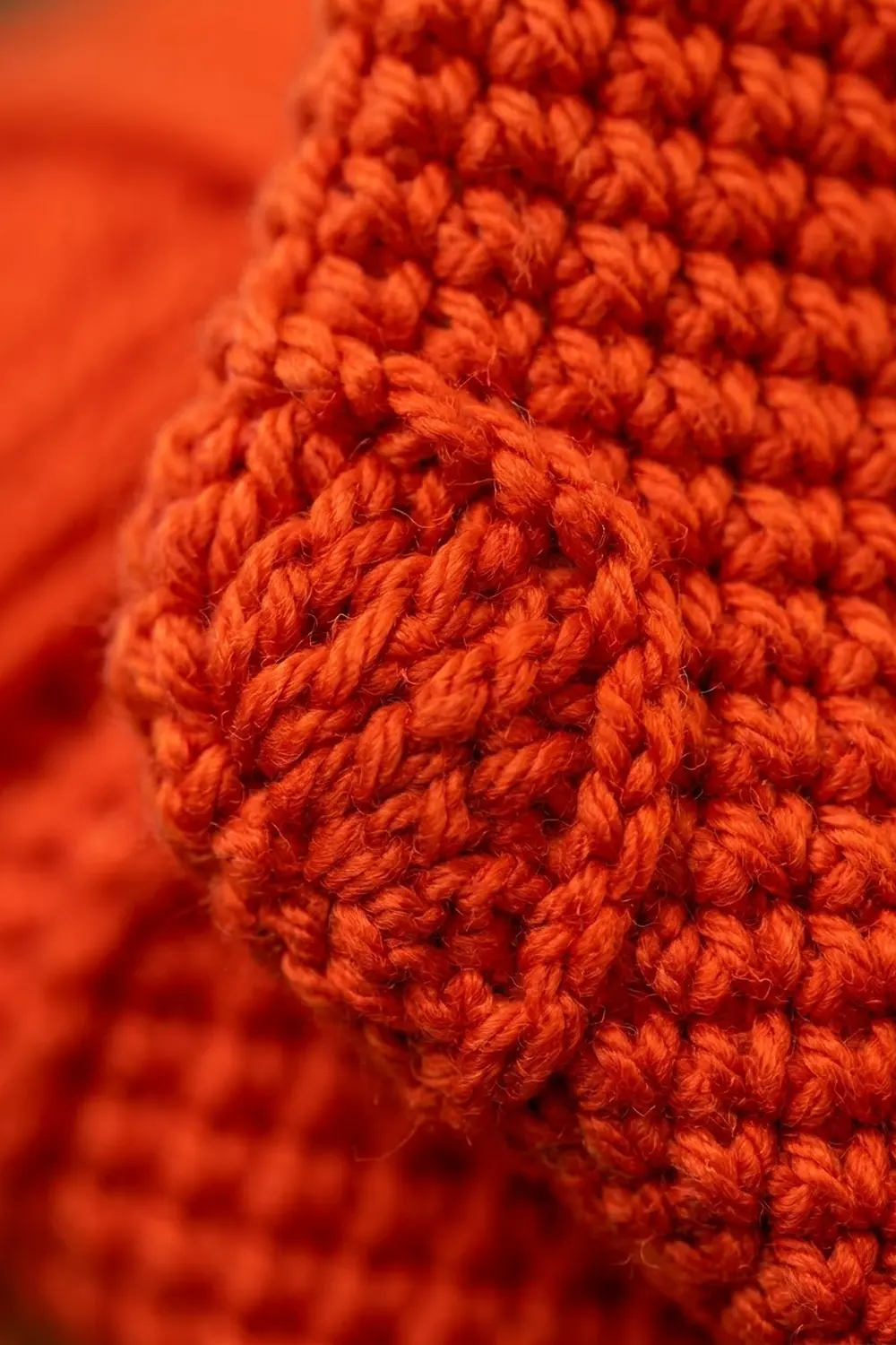 Close-up of vibrant orange-red crocheted or knitted textile showing detailed bobble stitch pattern and texture.