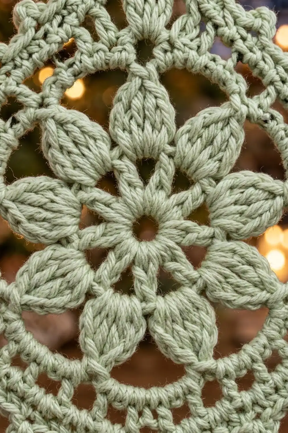 Close-up of intricate sage green crocheted lace with flower-like motifs and open pattern detail.