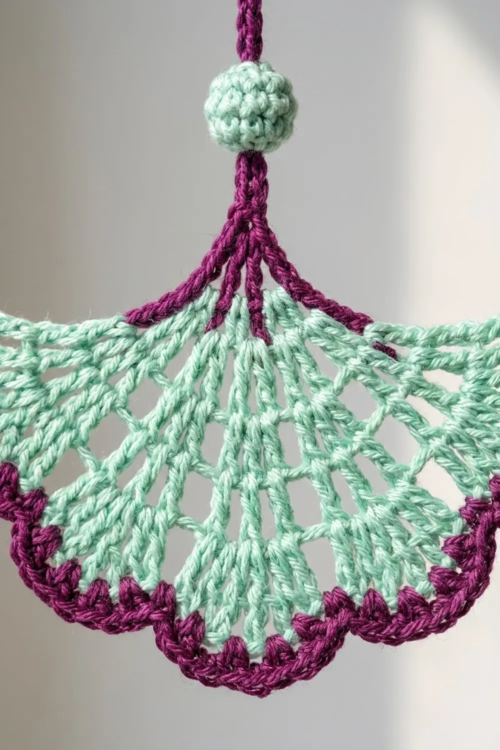 Crocheted ornament featuring a light green textured ball suspended above a burgundy and mint green fan-shaped pendant.