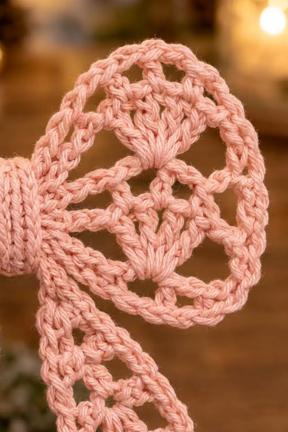 A pink crocheted rope forms an intricate looped pattern against a blurred warm-toned background.