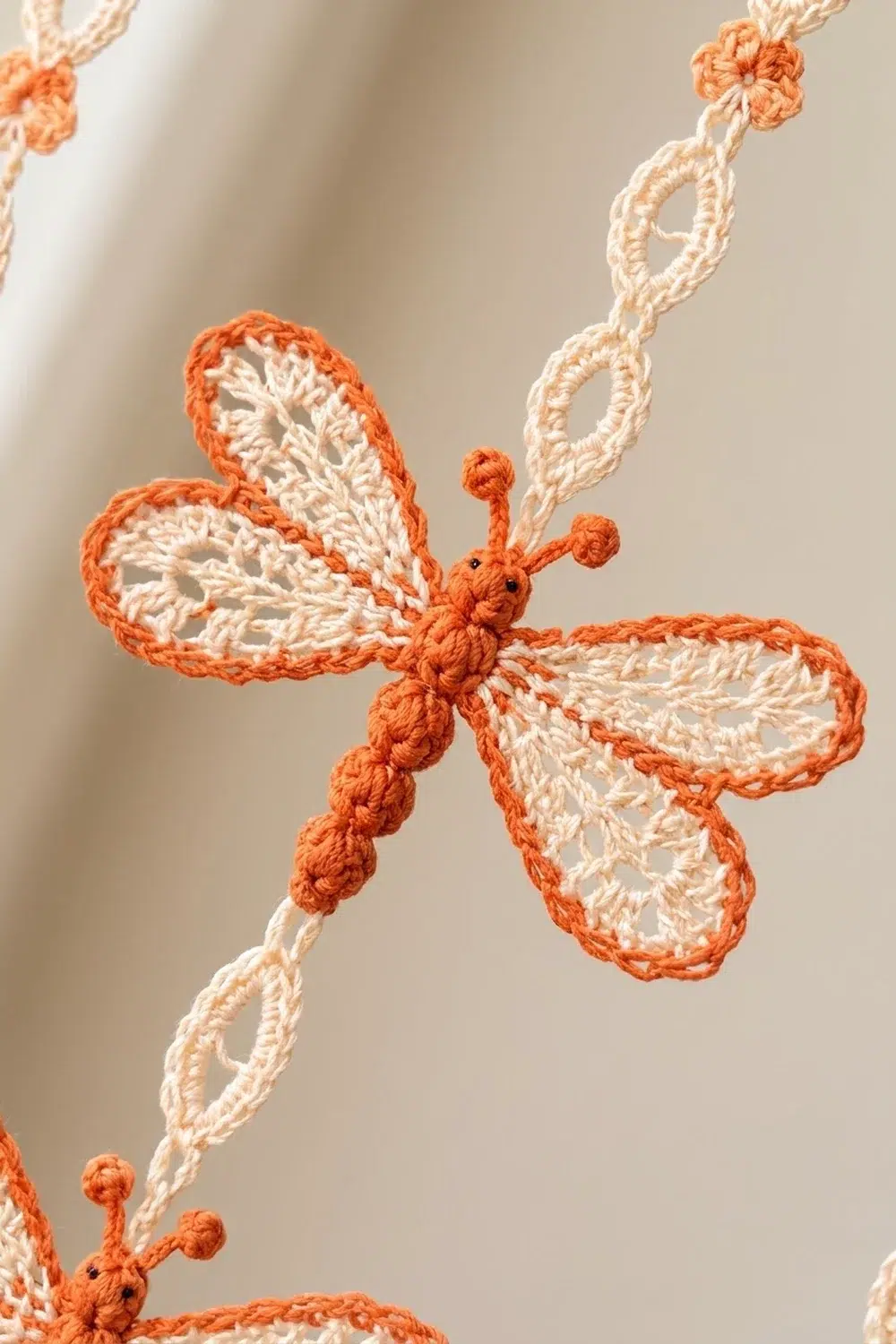 Crocheted orange and cream butterfly ornaments hanging from braided string against a soft beige background.