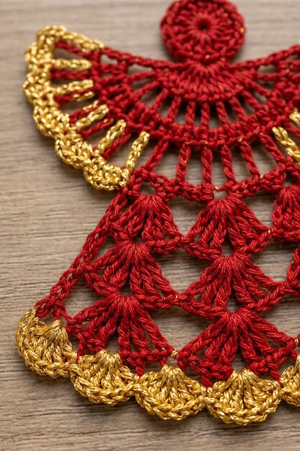 Red and gold crocheted lace doily with scalloped edges displayed on a wooden surface.