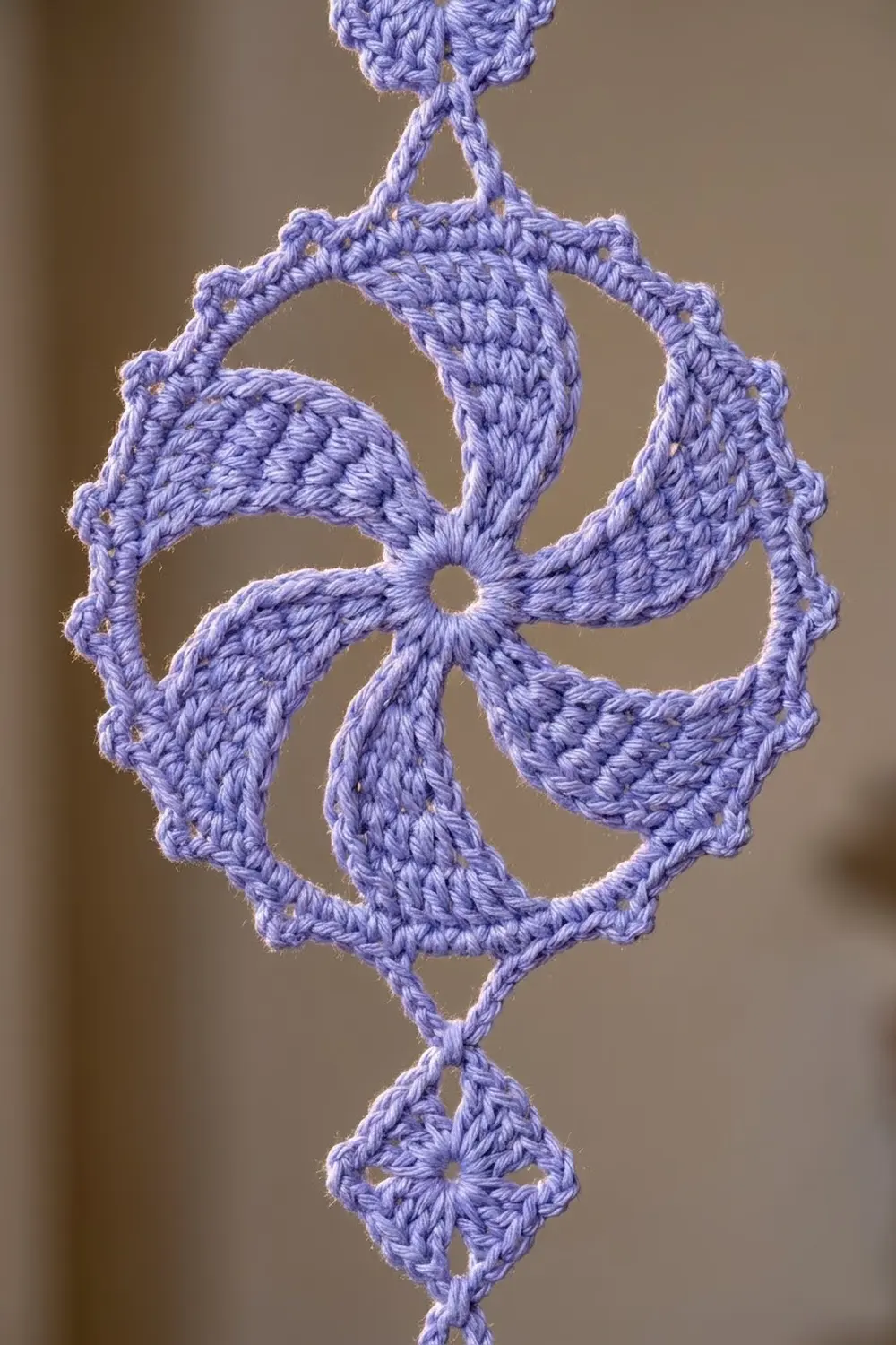 A delicate lavender crocheted ornament with four-petaled flower motifs hanging against a blurred neutral background.