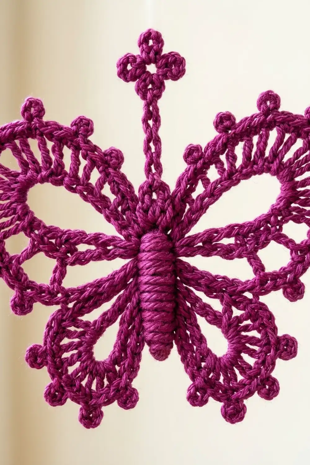 A crocheted purple snowflake ornament with intricate lace patterns and a cross topper displayed against a cream background.