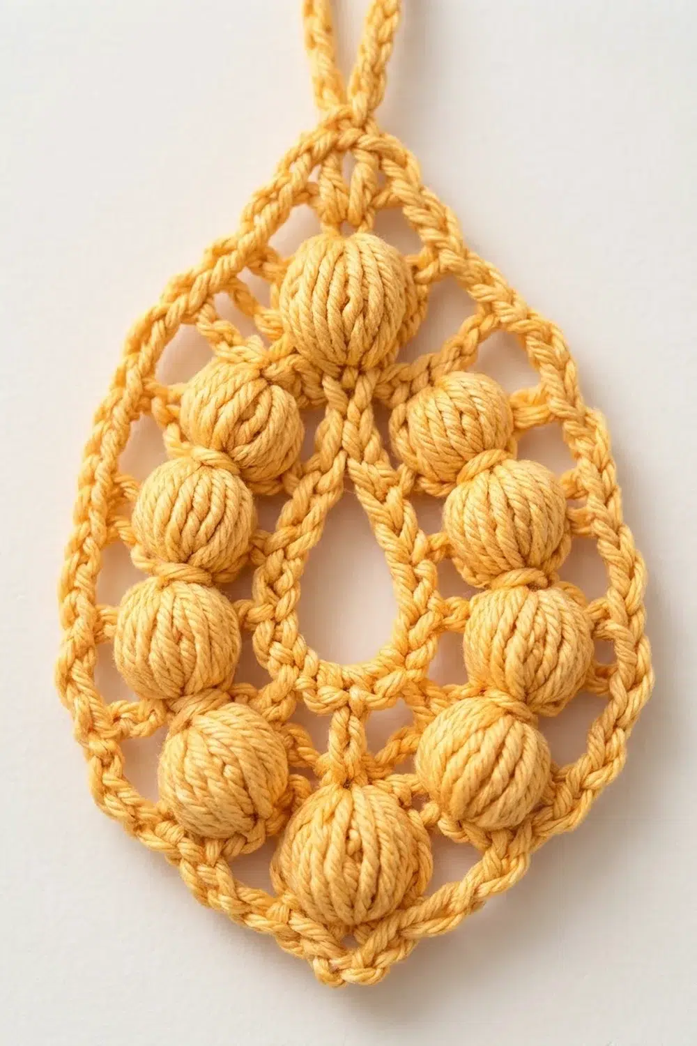 A golden yellow macramé ornament with wrapped rope beads arranged in a teardrop pattern against a white background.