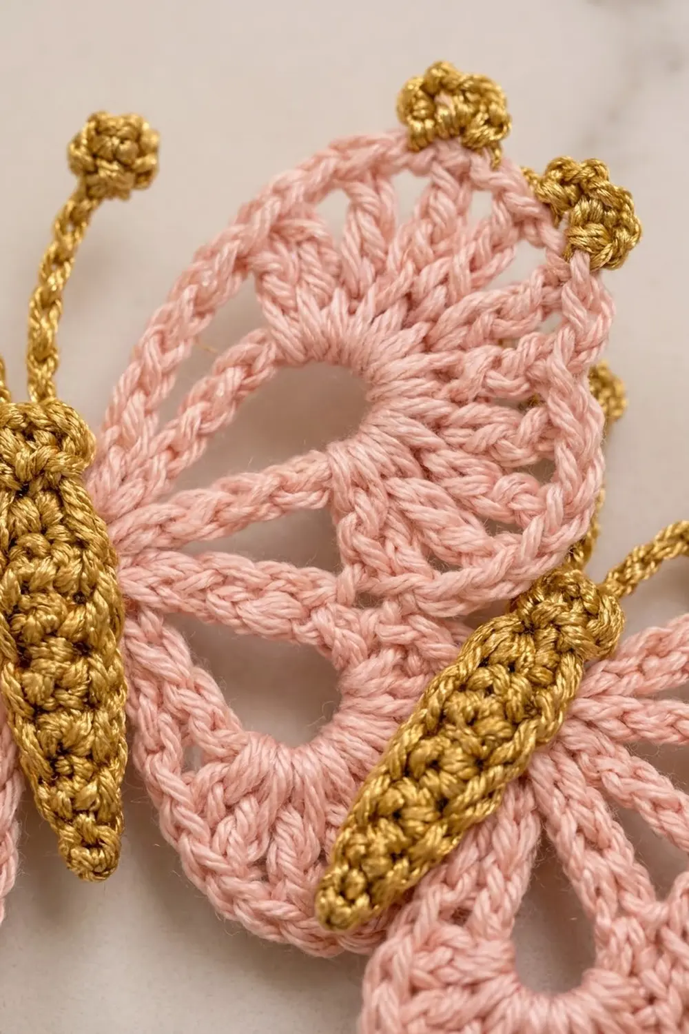 Close-up of pink braided rope with gold knot details arranged against a neutral beige background.