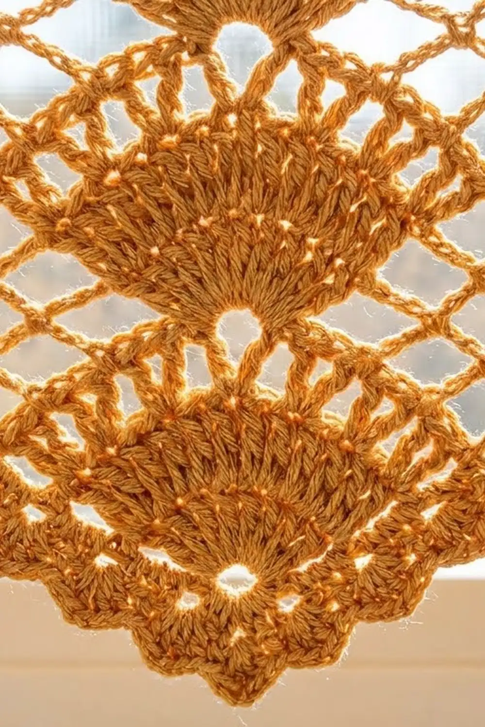 Close-up of golden-brown crocheted lace doily with open mesh pattern and textured center, backlit against white.