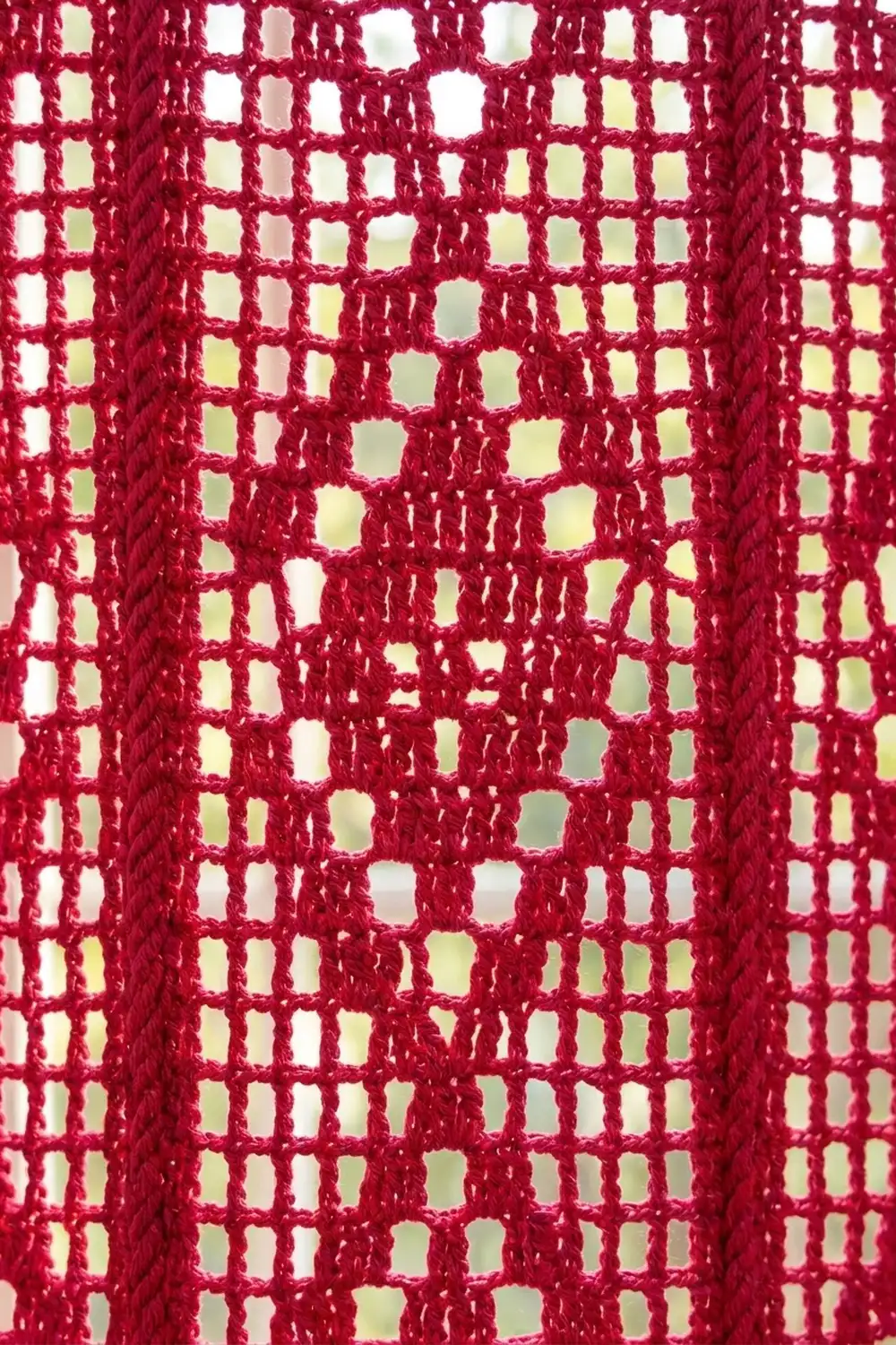 Close-up of red mesh fabric with a grid pattern of square openings, showing texture and light passing through.