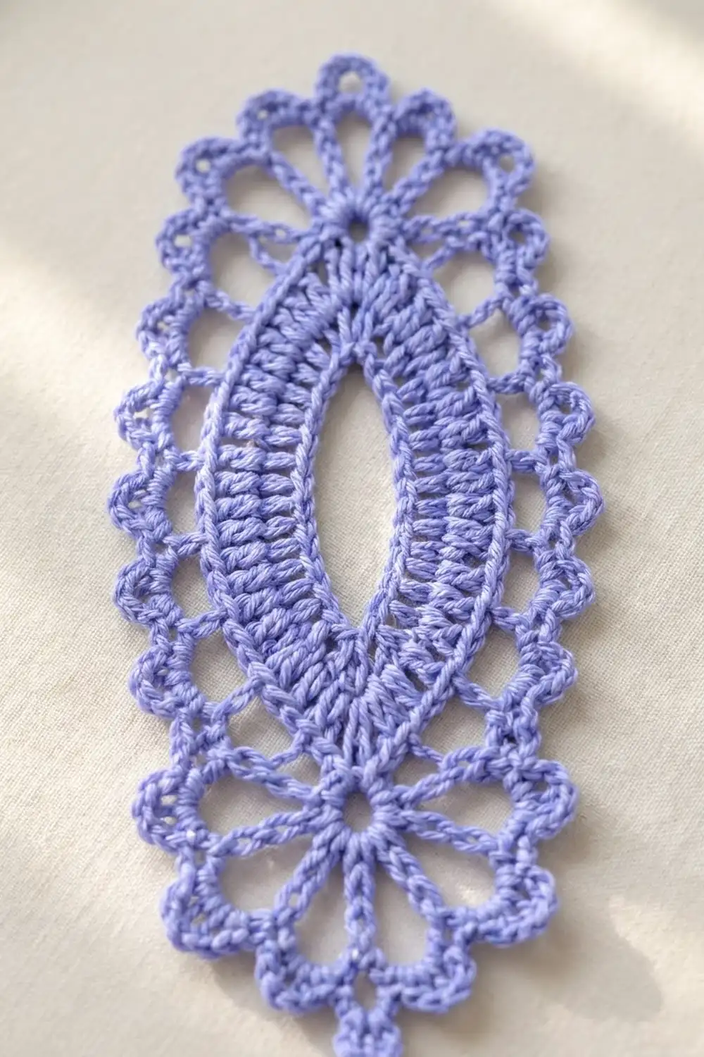 A delicate purple crocheted lace doily with an ornate floral pattern lies on a white fabric background.
