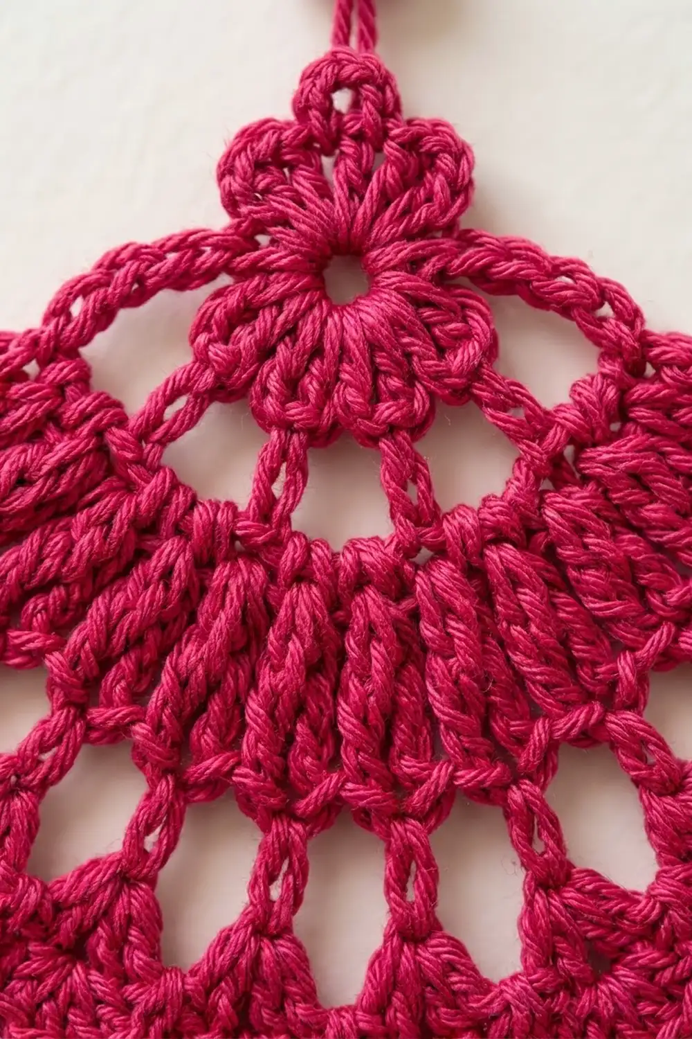 Close-up of a pink crocheted snowflake ornament with intricate looped details against a white background.