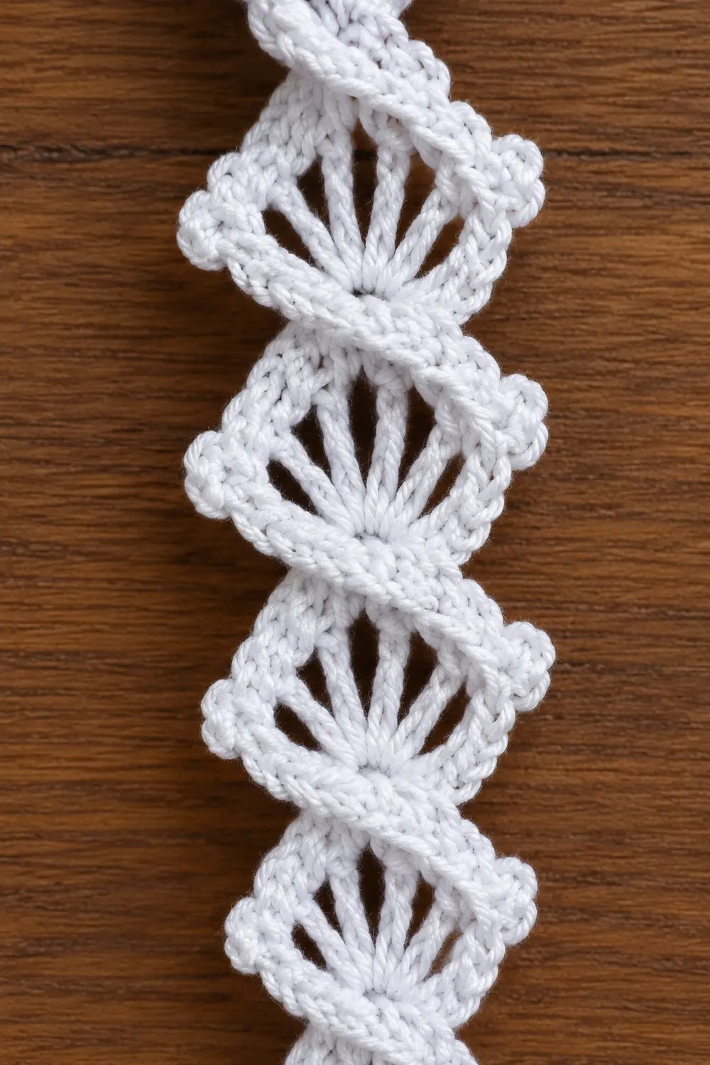 White macramé cord with repeated knot patterns creating decorative loops against a wooden surface.