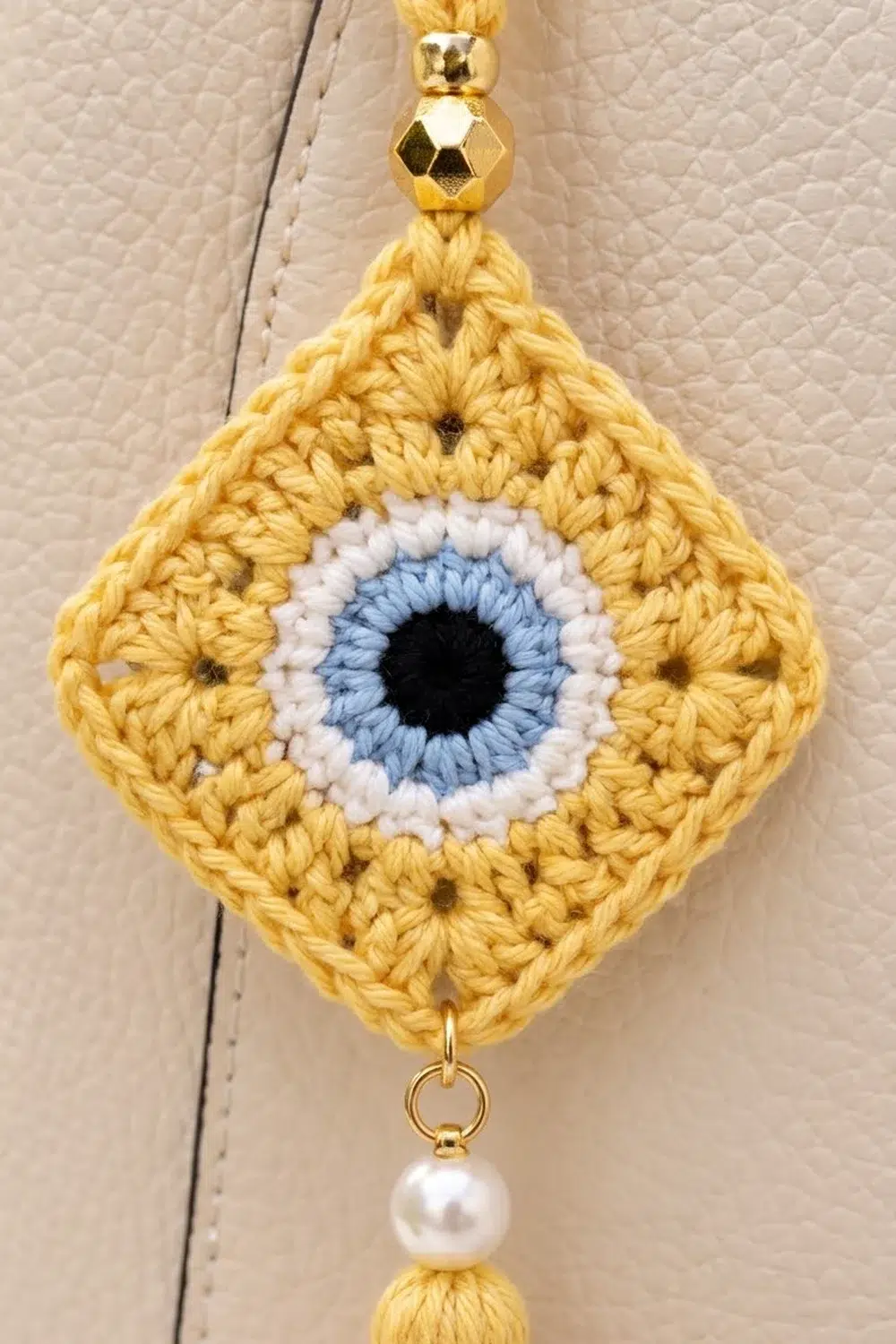 Crocheted yellow diamond charm with blue and white eye design, gold bead accents, and pearl dangle.