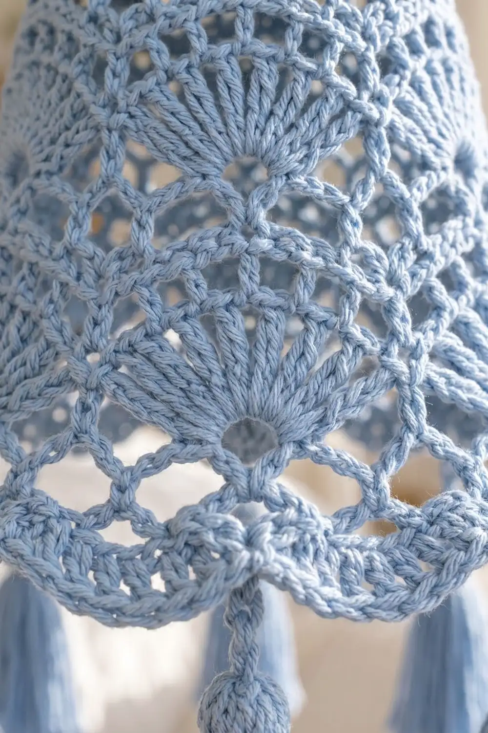 Close-up of light blue crochet lace fabric showing detailed shell stitch pattern with open mesh design.