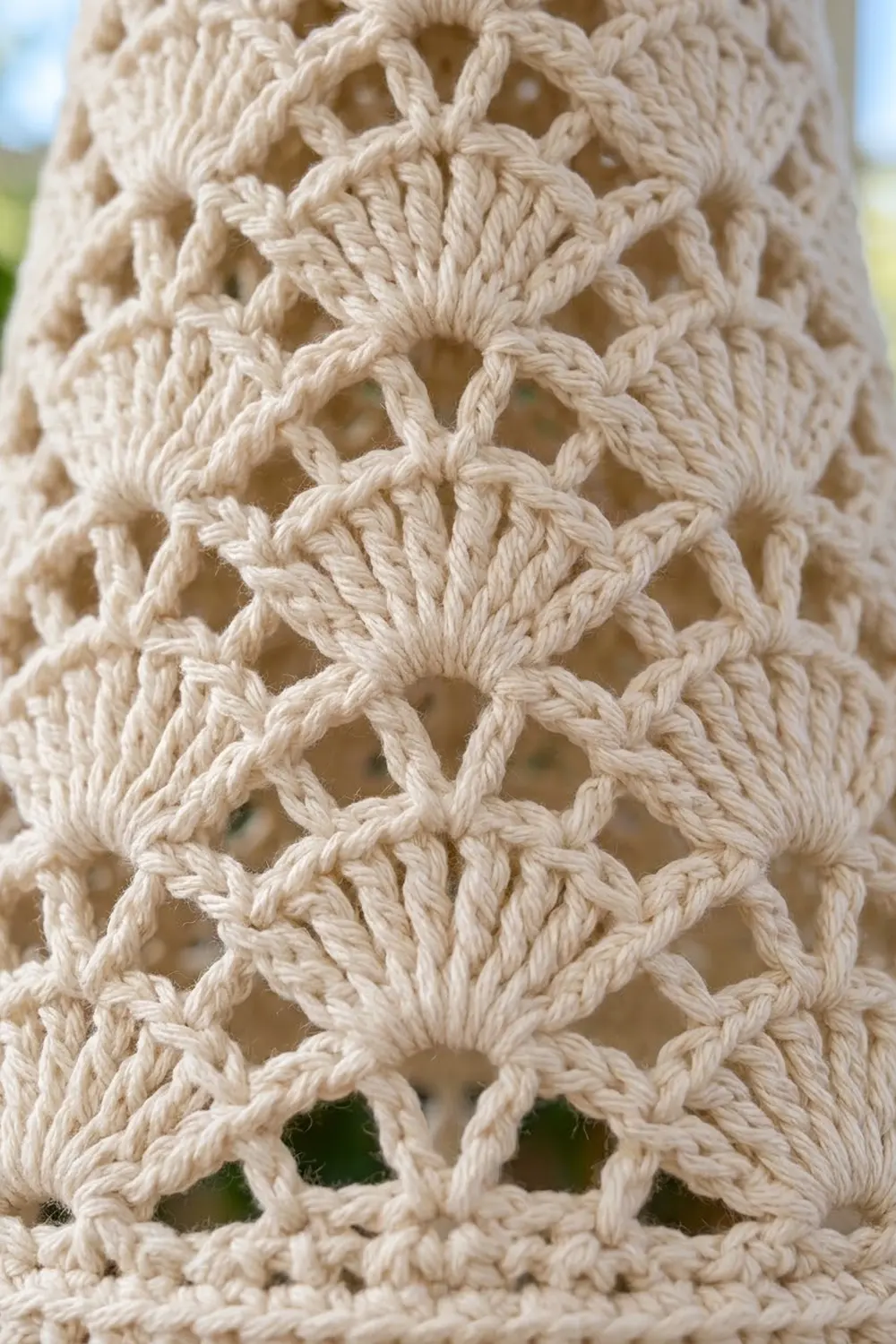 Close-up of cream-colored macramé textile showing detailed knotwork pattern with open diamond spaces.