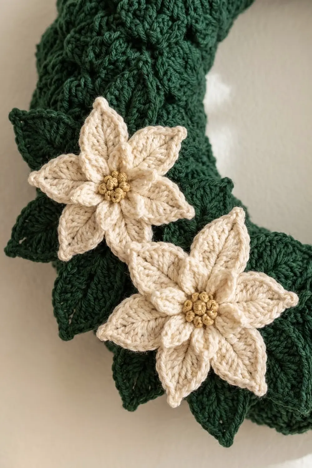 Crocheted cream-colored flowers with golden centers attached to a green cable-knit knitted garment.