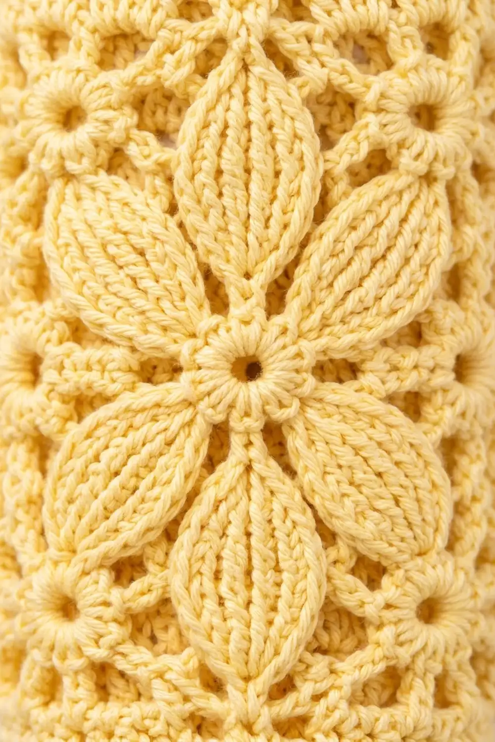 Close-up of pale yellow crocheted fabric showing an intricate floral motif with detailed textured stitching.