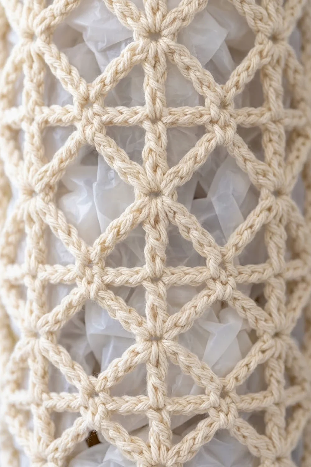 Close-up of cream-colored macramé knotwork with diamond patterns layered over white sheer fabric backdrop.