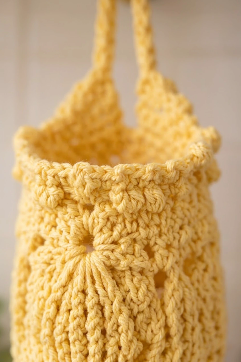 Close-up of a yellow crocheted bag showing textured stitching detail with two rope handles.
