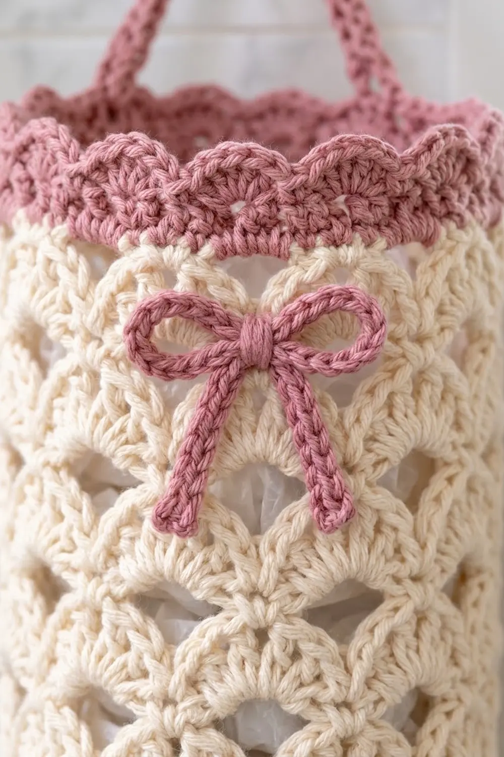 Close-up of a crocheted tote bag featuring a pink bow appliqué on cream-colored textured fabric.