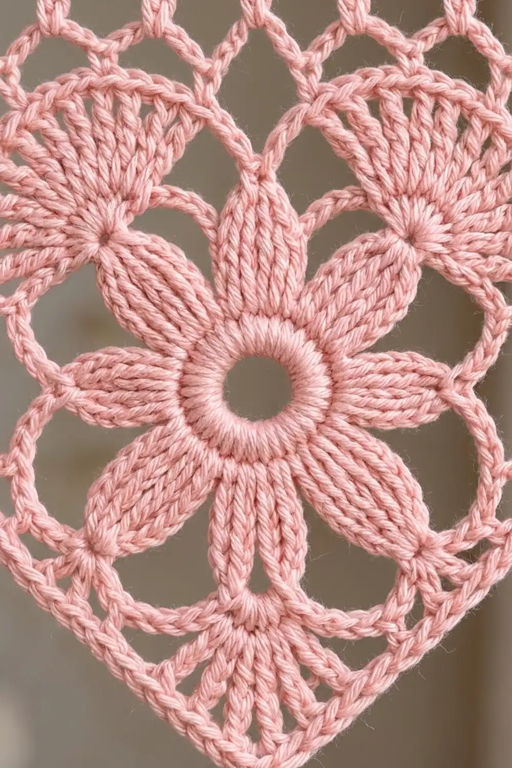 Close-up of delicate pink crochet lace featuring a floral motif with open-work design against neutral background.