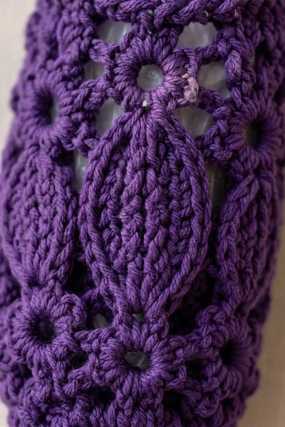 Close-up of purple crocheted lace fabric showing intricate open-work pattern with repeating loops and gaps.