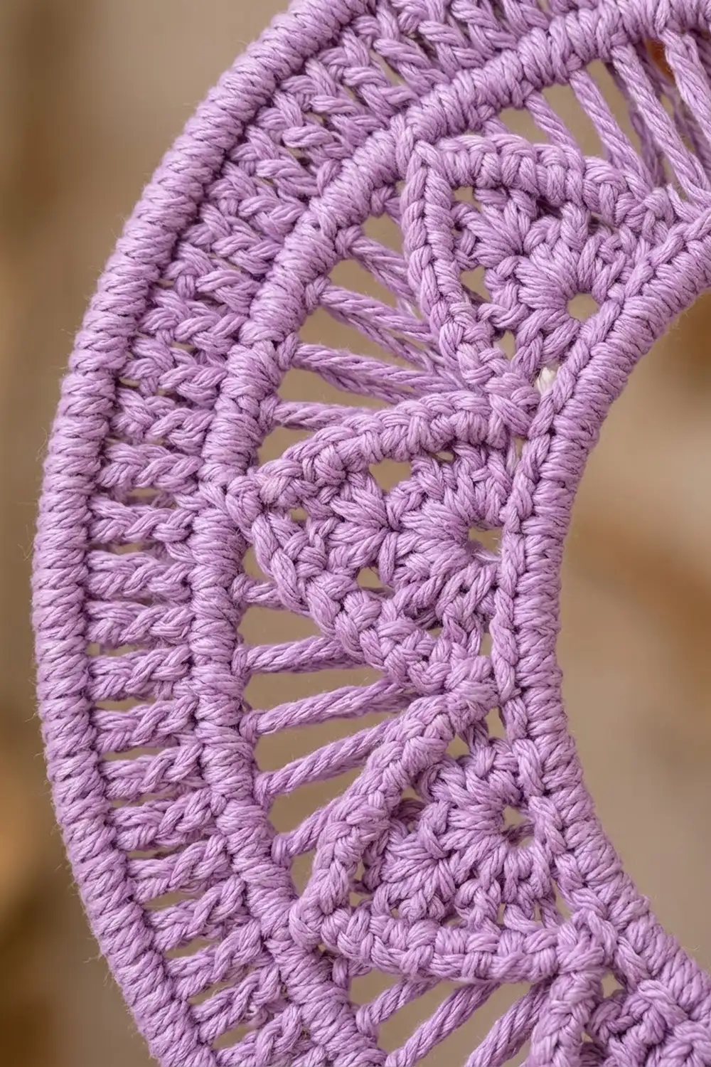 Close-up of lavender crocheted lace with intricate openwork pattern and textured stitching against a soft neutral background.