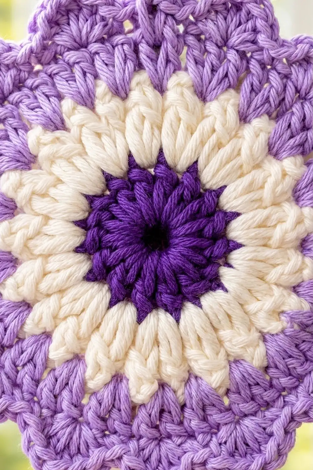 Close-up of a crocheted flower with purple outer petals, cream middle petals, and deep purple center.