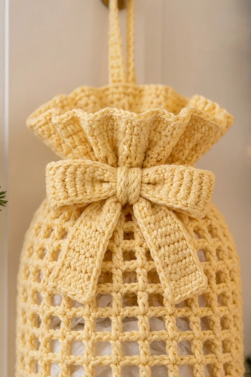 A cream-colored crocheted ornament with an open lattice pattern and decorative bow hangs from a golden cord.