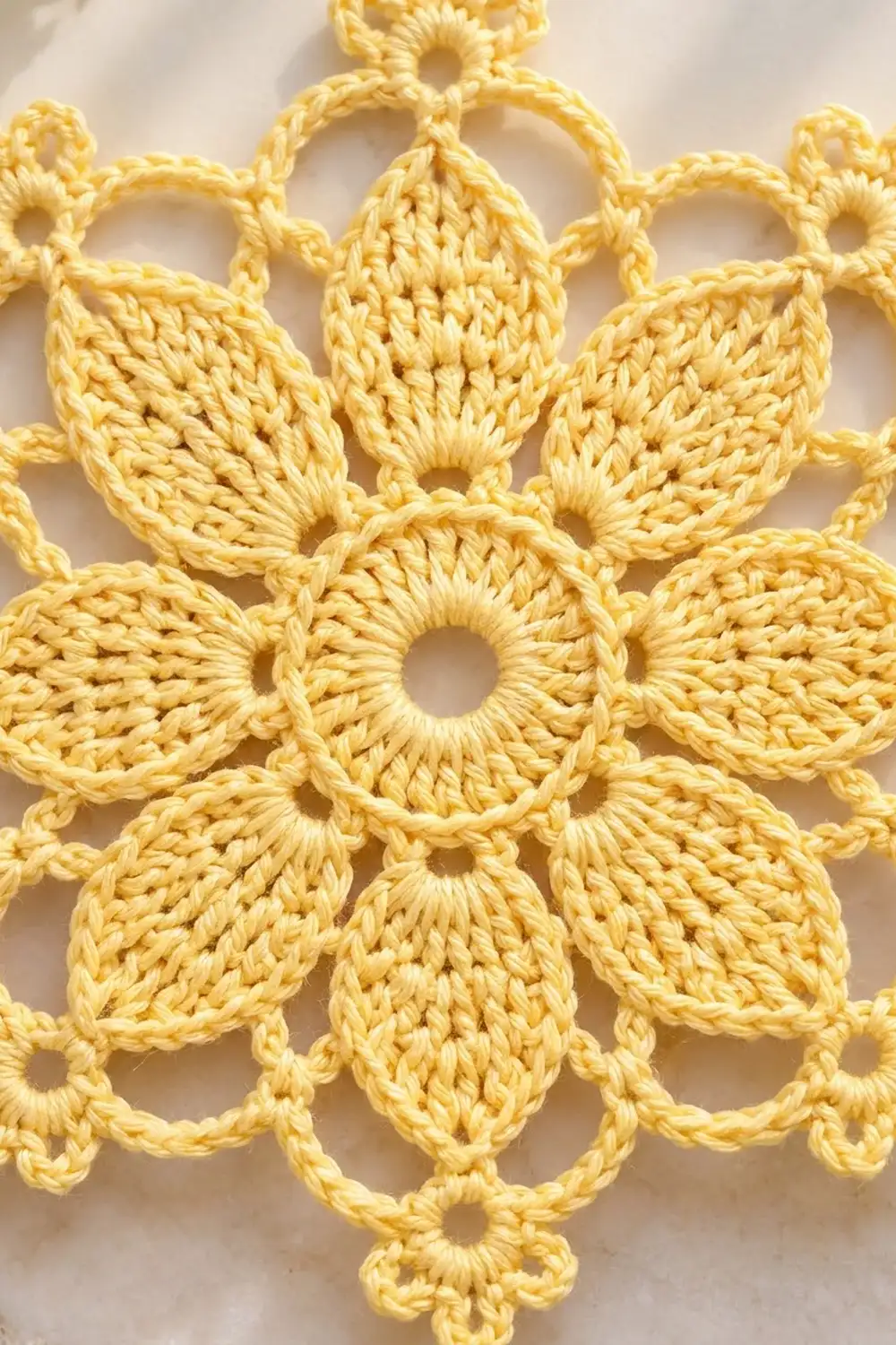 Close-up of a yellow crocheted lace doily with intricate flower motifs and open lacework on white background.