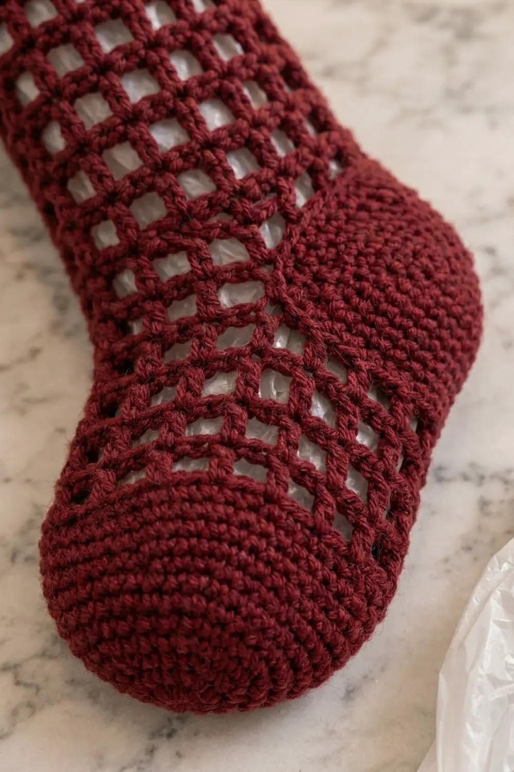 Burgundy crocheted sock with lattice pattern detail displayed on marble surface.