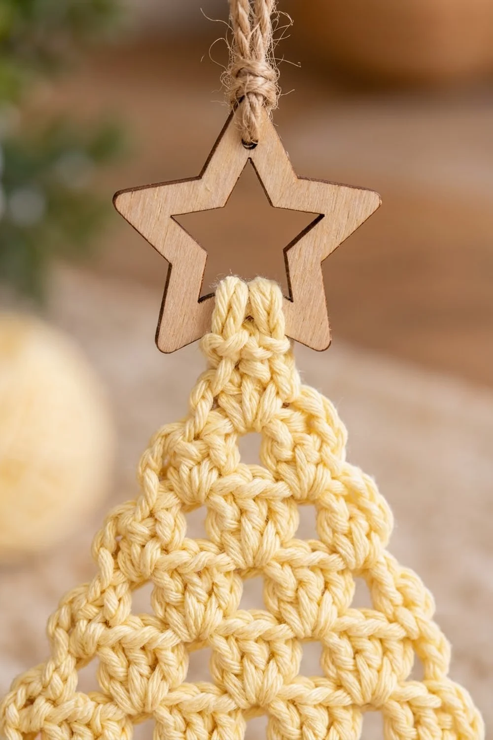 A cream-colored crocheted Christmas tree ornament hangs from a wooden star topper with twine.