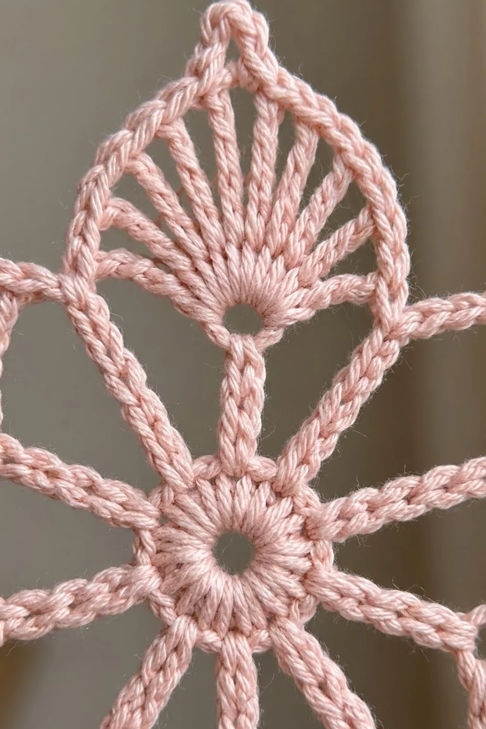 Close-up of a pink twisted rope arranged in a symmetrical knot pattern against a neutral beige background.