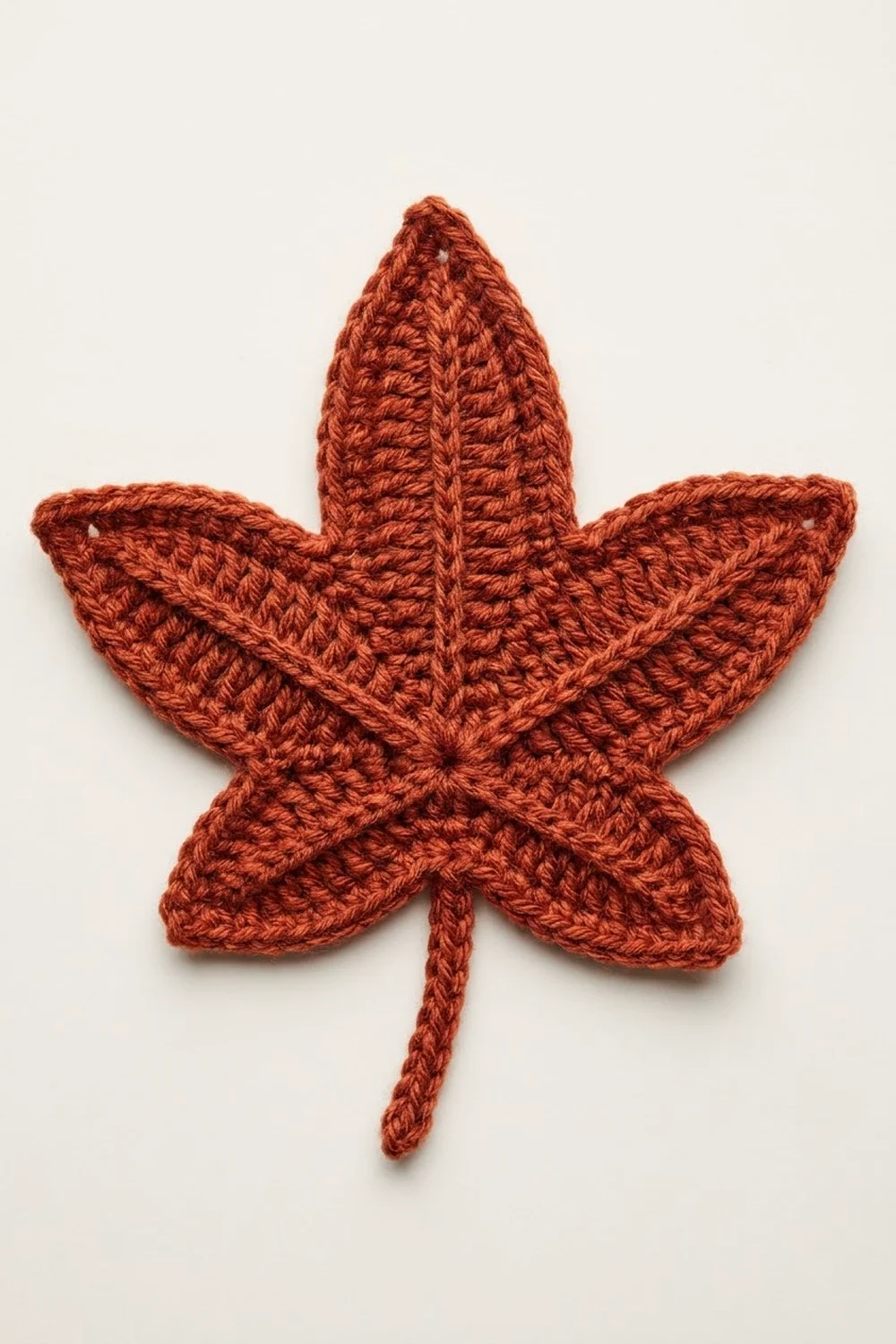 A crocheted maple leaf in burnt orange yarn with a textured stitch pattern against a white background.