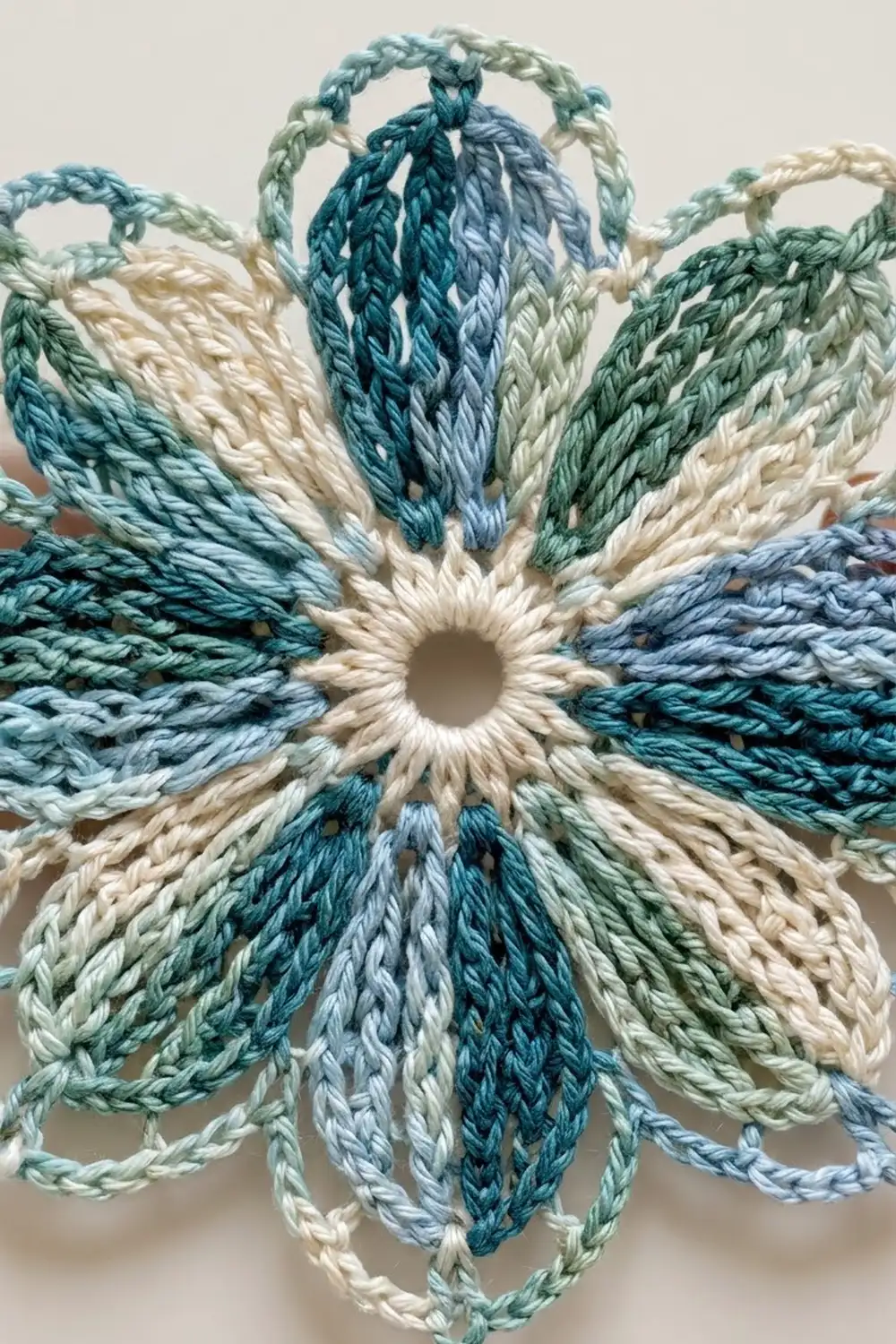 Braided rope flower ornament with cream, teal, and gray twisted petals arranged in a circular pattern.