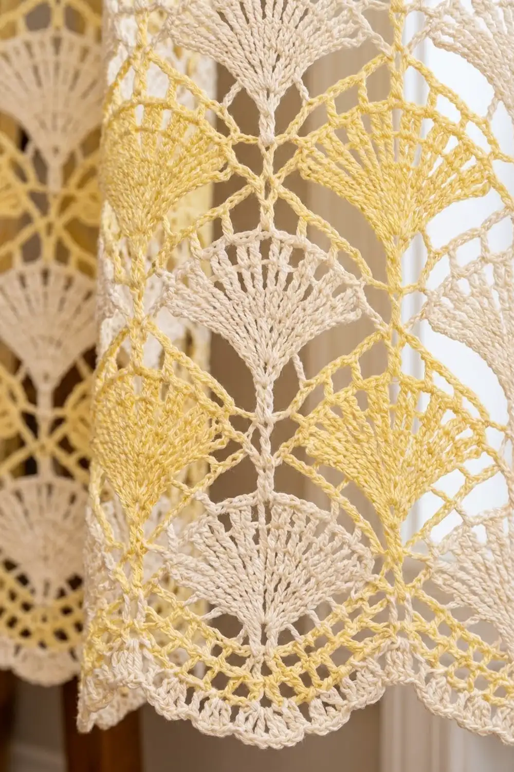 Close-up of delicate lace trim alternating cream and pale yellow crocheted fan motifs with openwork pattern.