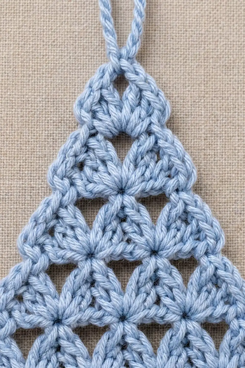 Light blue crocheted Christmas tree ornament with open lacework pattern hanging from twisted cord.