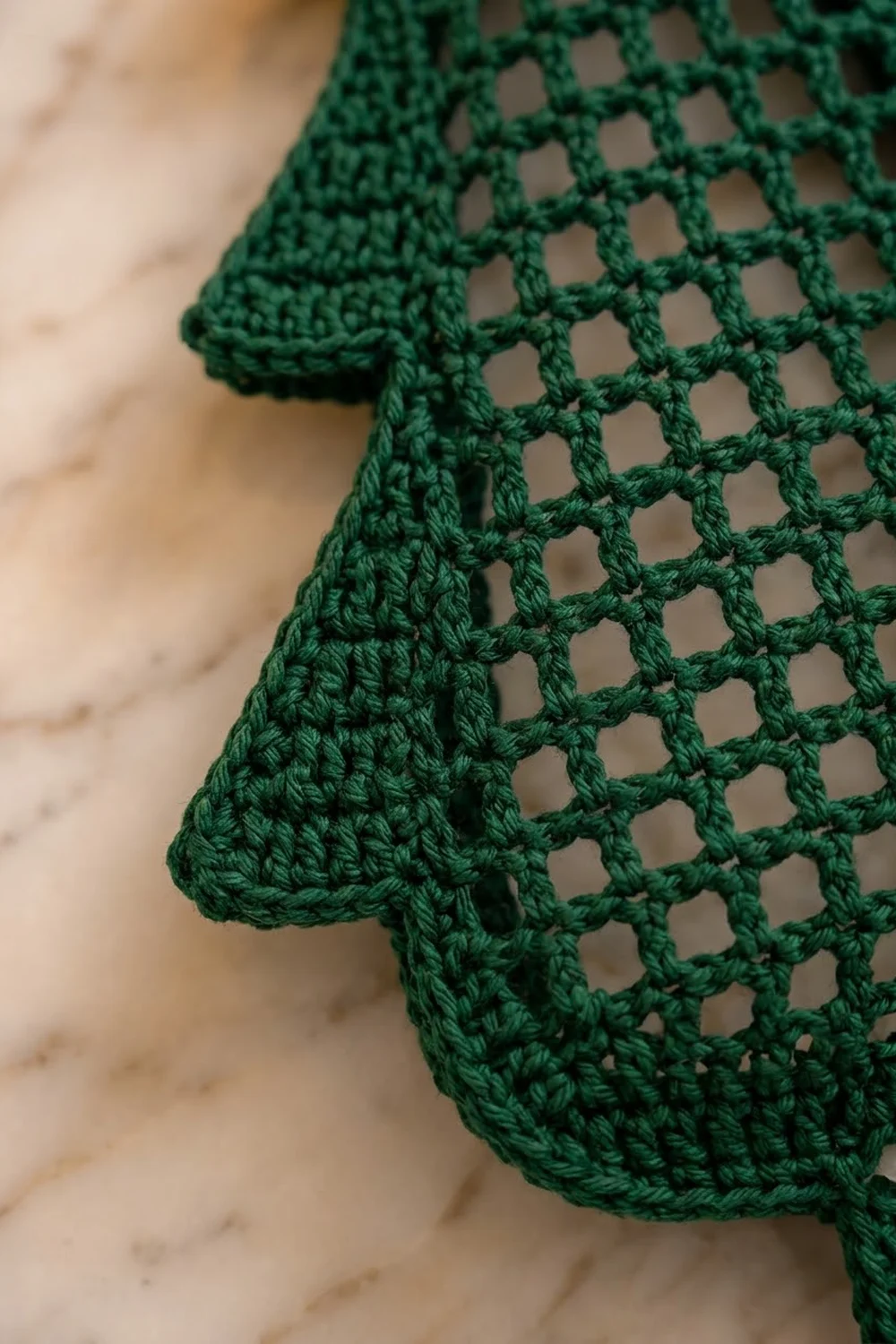 Close-up of a green crocheted shawl or wrap showing detailed lacy stitch pattern on marble surface.