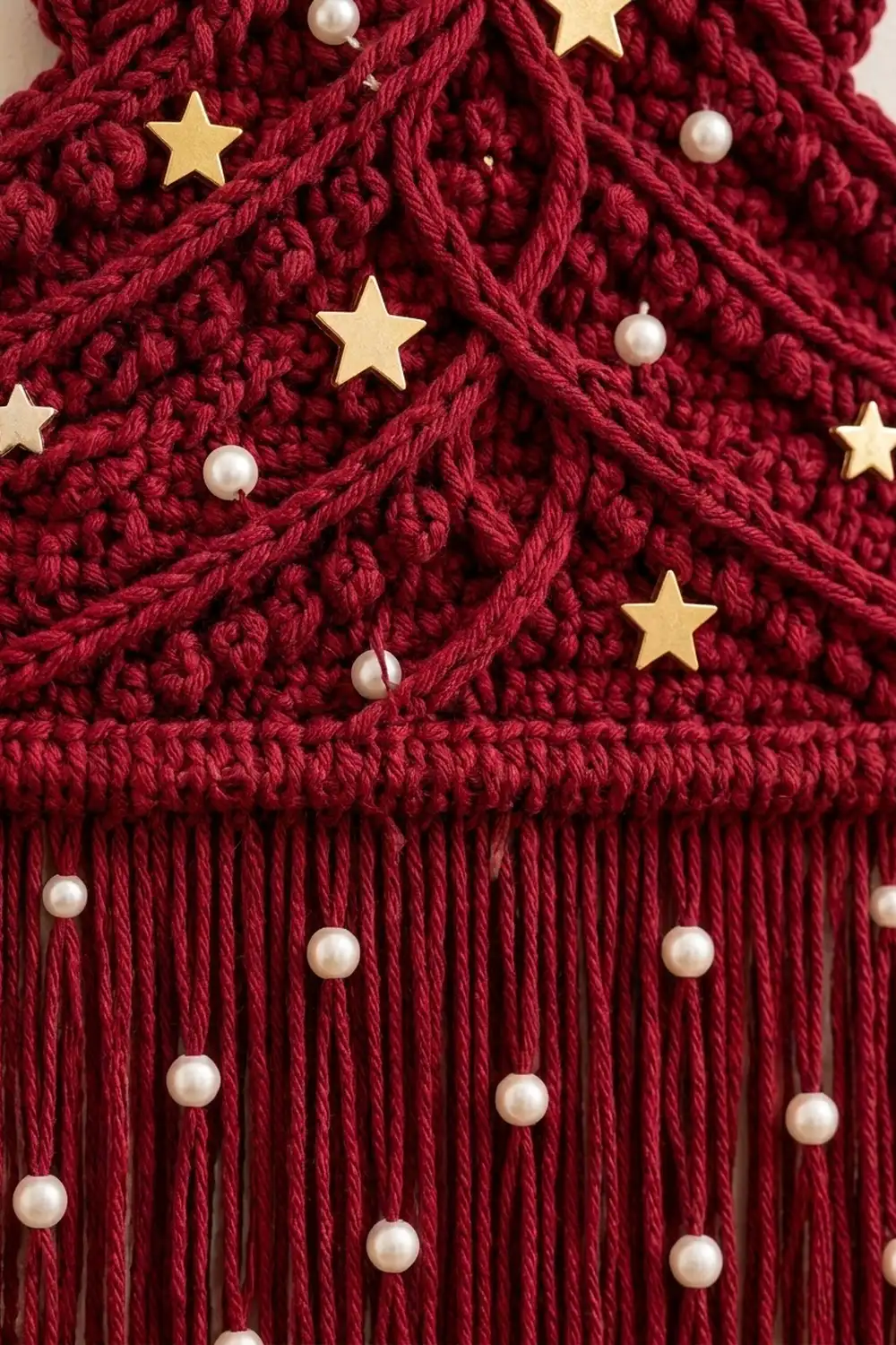 Deep burgundy knit fabric adorned with gold stars and pearl beads as holiday decoration.