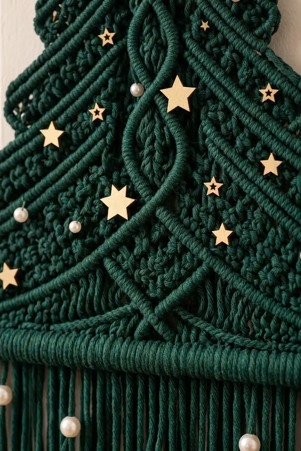A dark green macramé Christmas tree ornament decorated with gold stars and pearl beads.