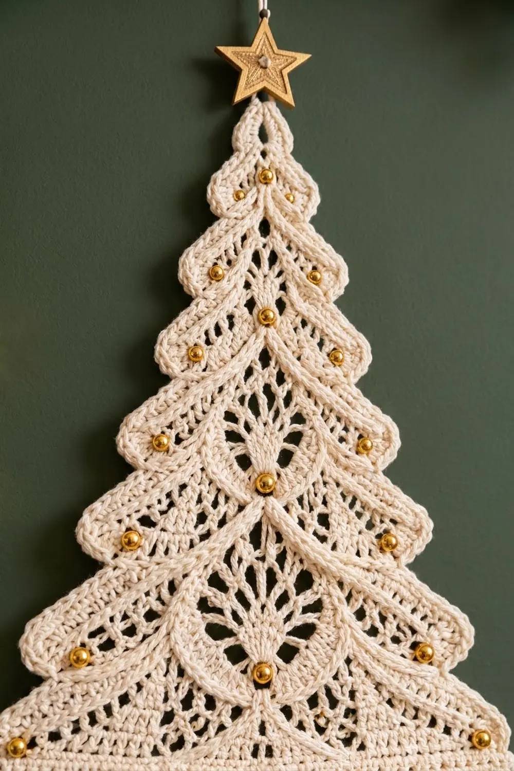 Crocheted cream-colored Christmas tree ornament with gold beads and wooden star topper against green background.
